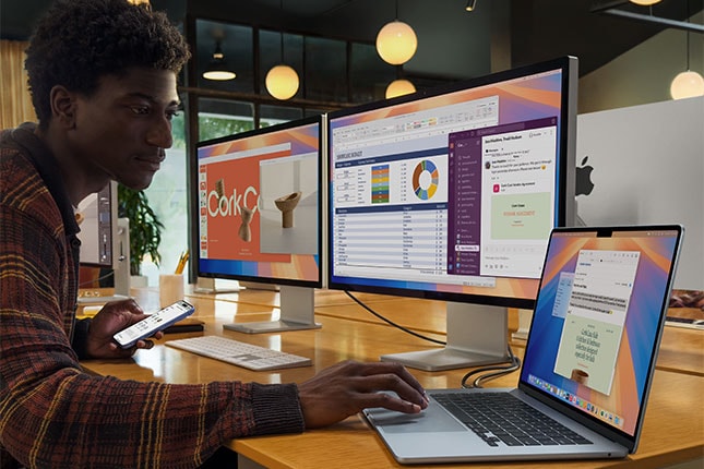 Team member working in modern office with iMacs, MacBook and iPhone at desk